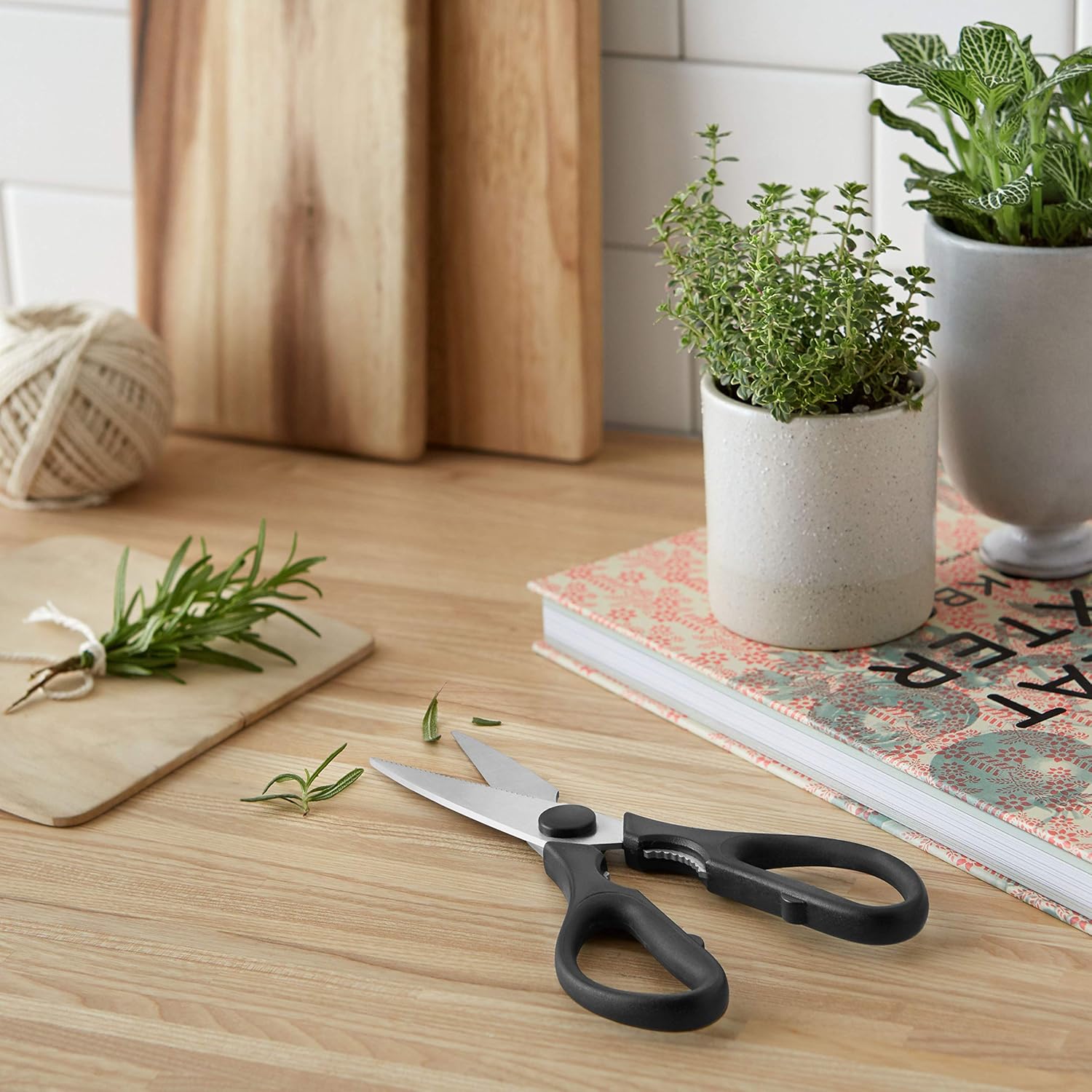 Tijeras de cocina Amazon Basics sobre una mesa de madera junto a hierbas aromáticas frescas
